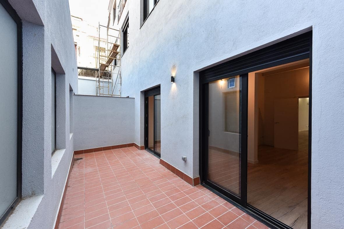 Patio interior rehabilitado, con el pavimento cerámico rojo, las correderas nuevas de aluminio negro y una estancia iluminada al fondo