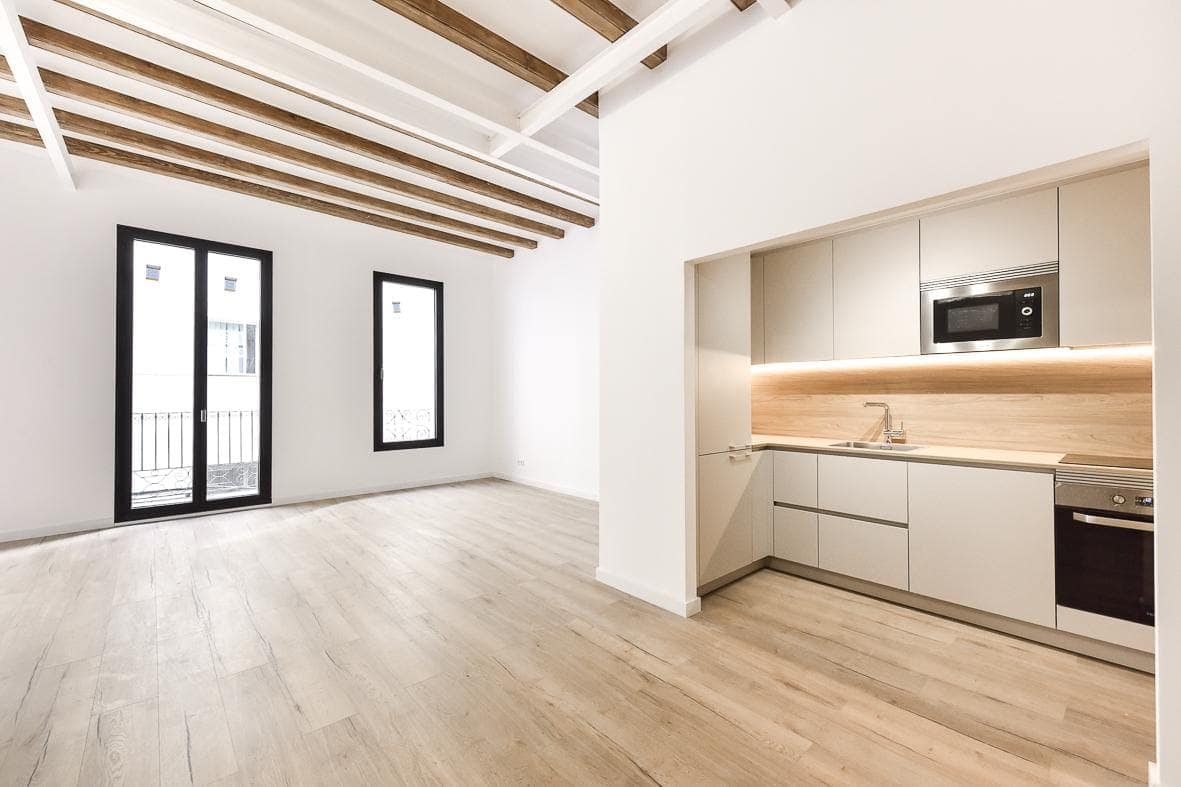 Salón-cocina de una de las viviendas de Granada del Penedès, con el techo de vigas de madera restauradas y balconeras negras