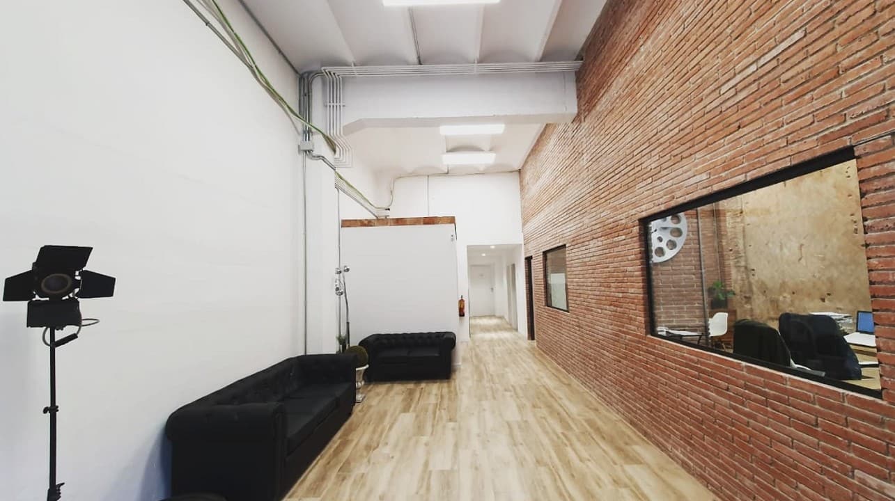 Zona de estar con sofás chester, pared de ladrillo visto y vistas a una de las oficinas acristaladas