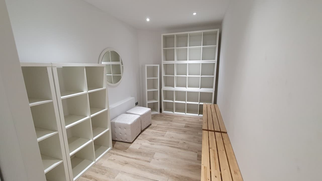Interior de uno de los vestuarios, con estanterías abiertas, banco de madera y espejo redondo