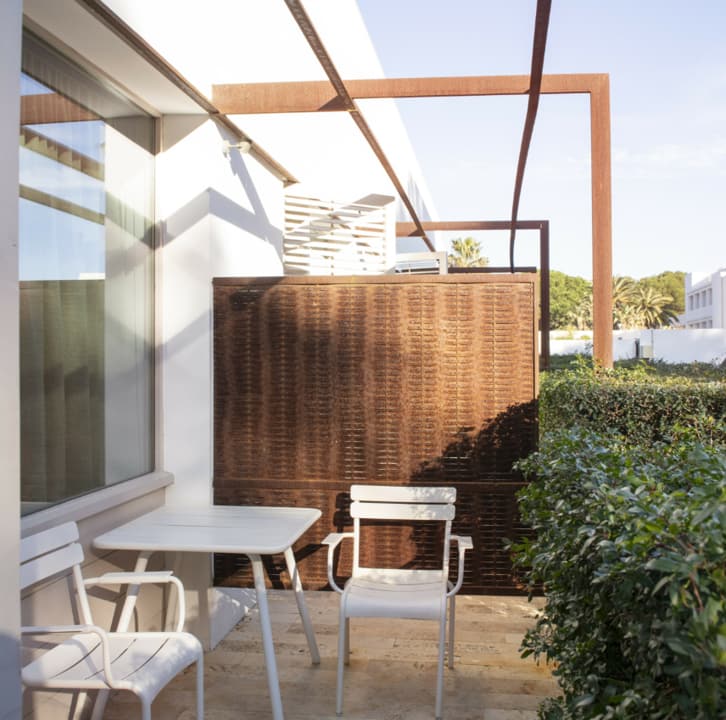 Terraza privada con pérgola y celosía de acero corten, con mesa y sillas blancas