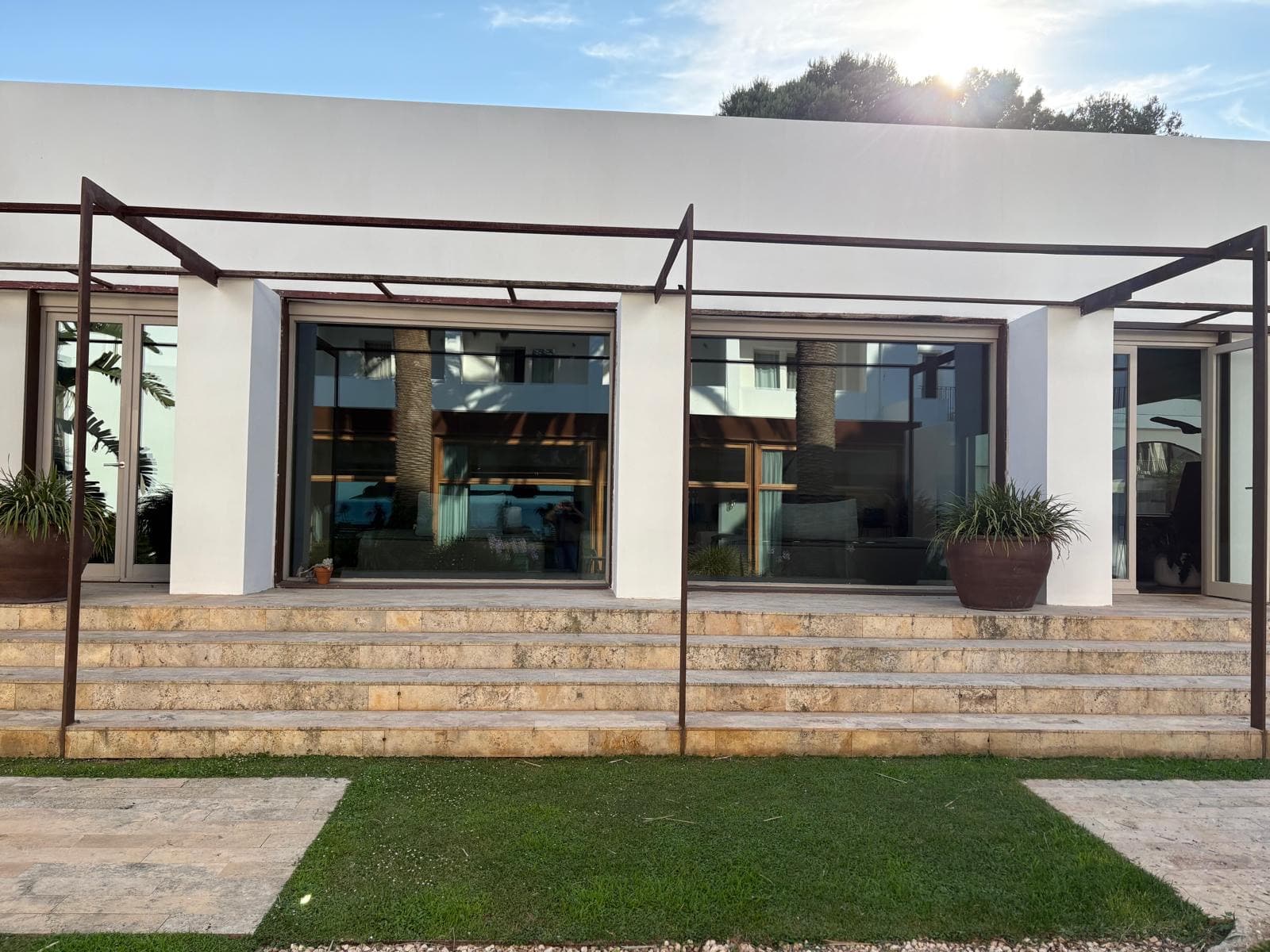Porche con pérgola de acero corten y escalera de piedra hacia el jardín