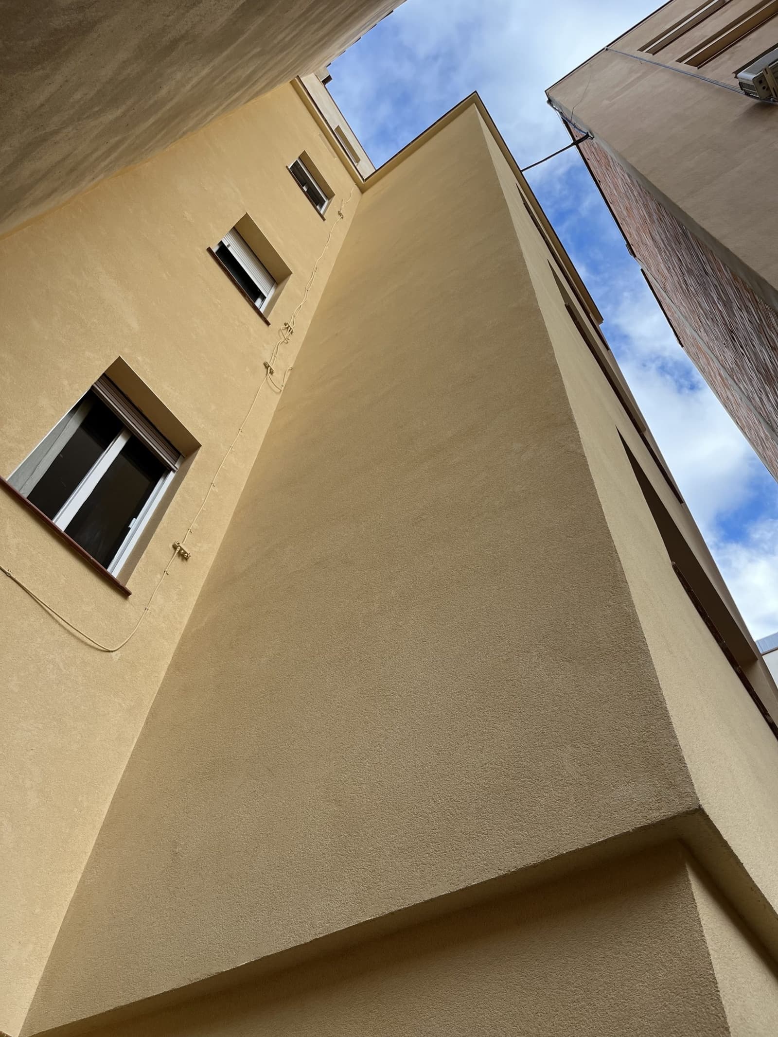El patio de luces en contrapicado, con la esquina de la fachada rehabilitada y el cielo entre los edificios