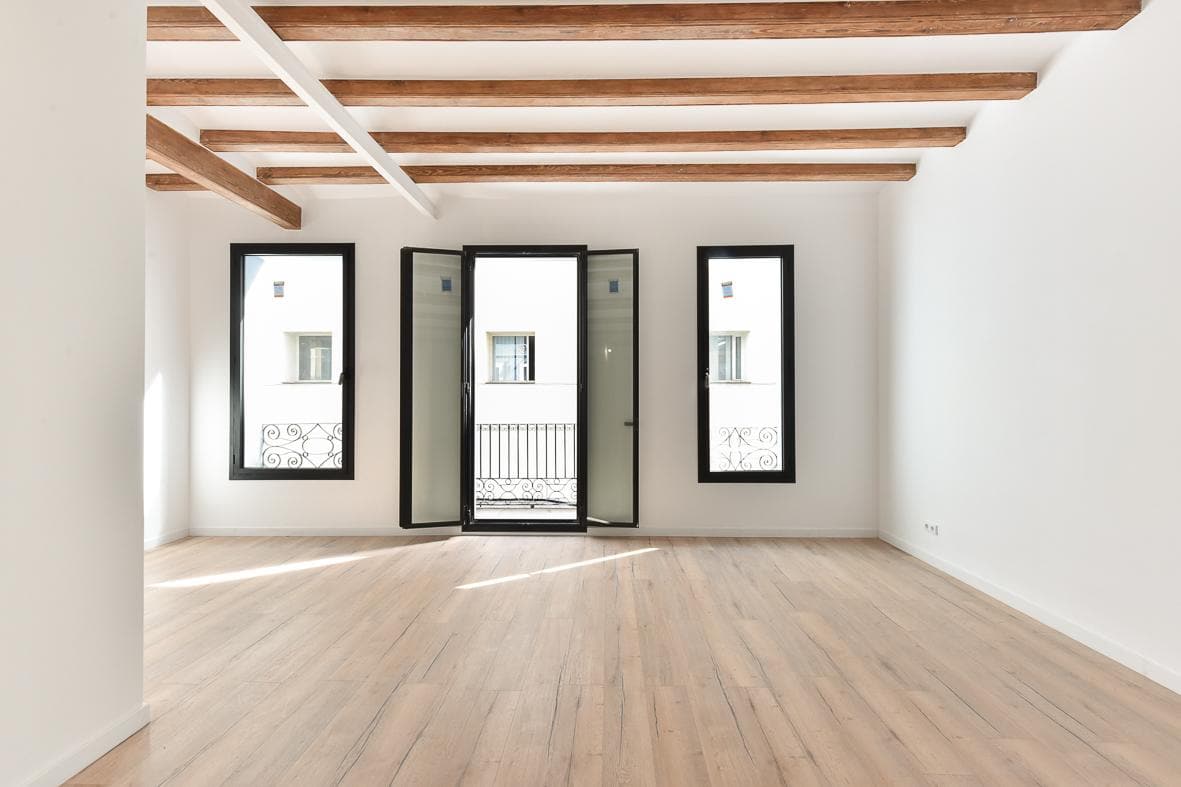 Estancia con las tres balconeras de carpintería negra bajo el techo de vigas de madera restauradas