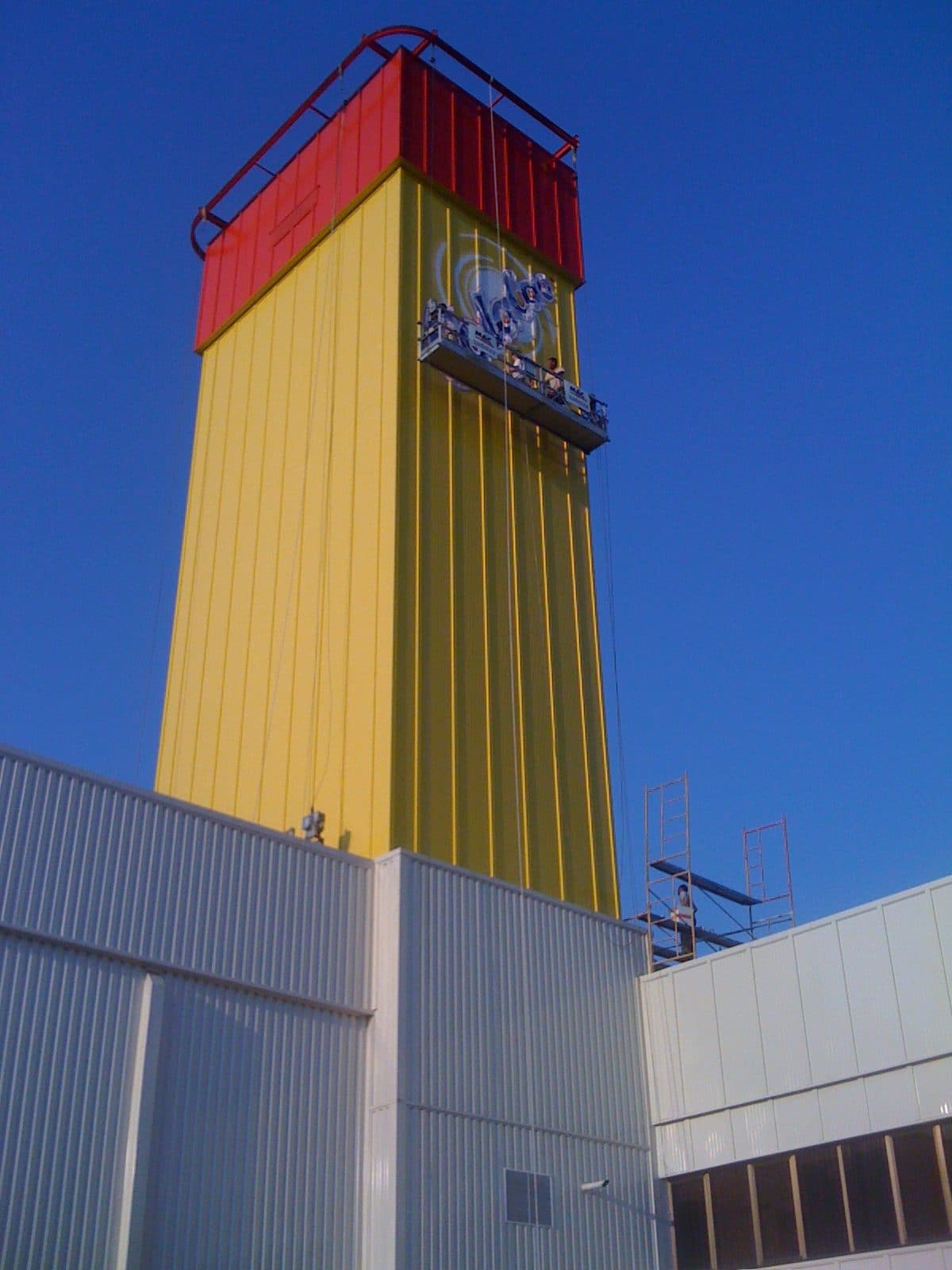 Dos operarios aplicando el logotipo desde una góndola colgada de la torre ya pintada