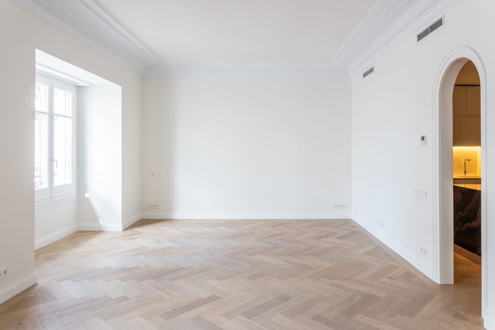 Salón del Piso Muntaner con suelo de espiga de roble, molduras de escayola restauradas y arco de paso a la cocina
