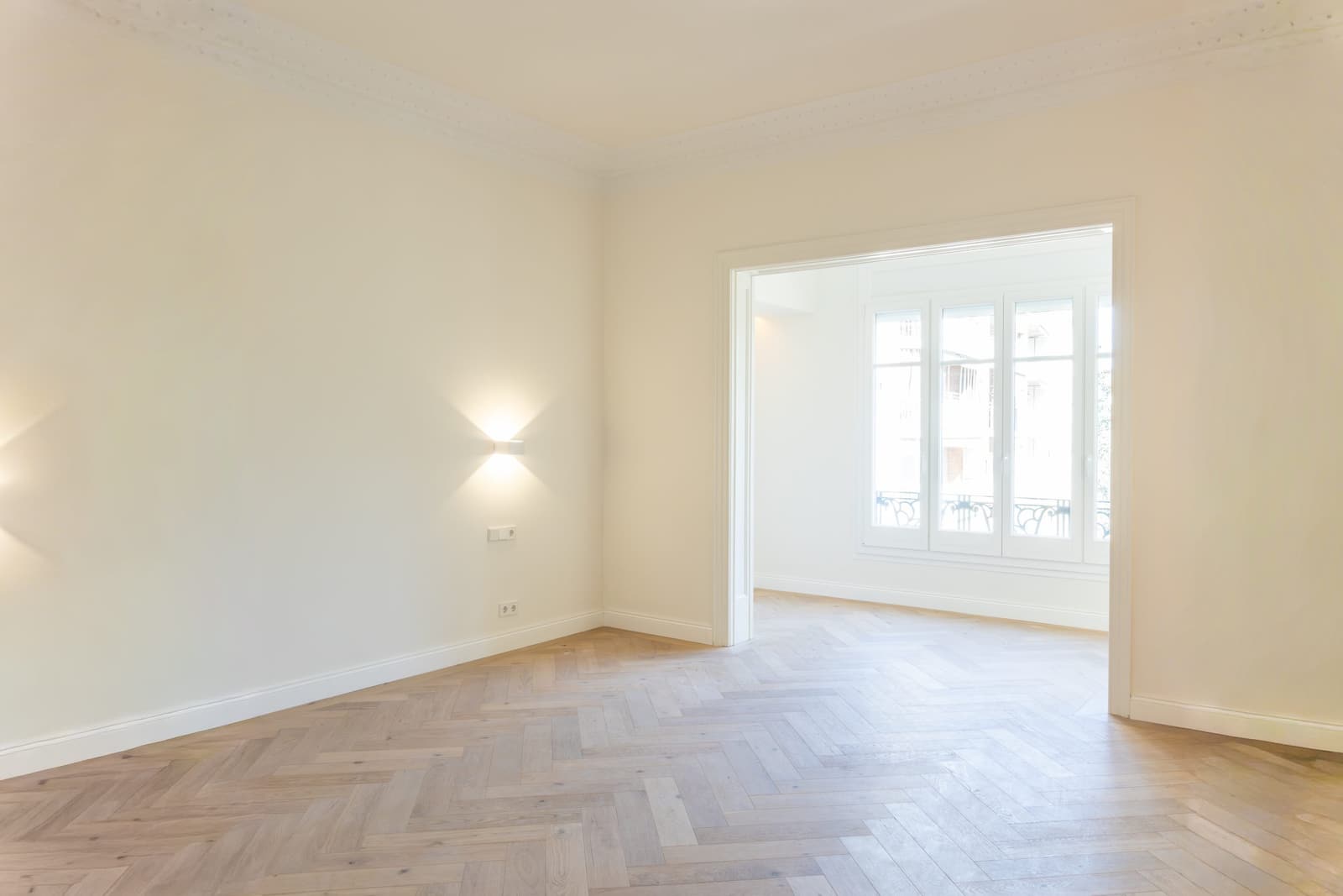 Habitación con aplique de pared y paso a la estancia con balcón, sobre suelo de espiga de roble