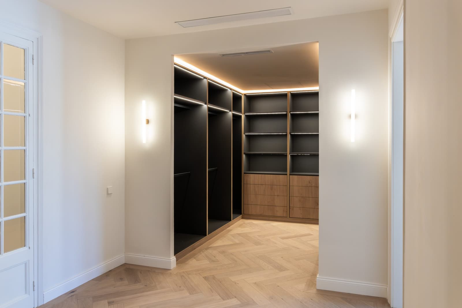 Vestidor abierto con módulos negros retroiluminados y cajonera de roble