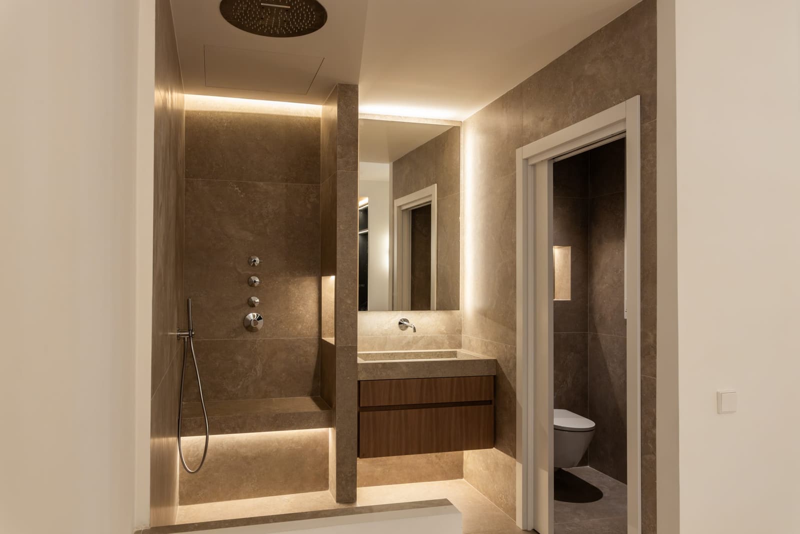 Baño principal revestido en porcelánico con ducha de obra, banco corrido y aseo independiente