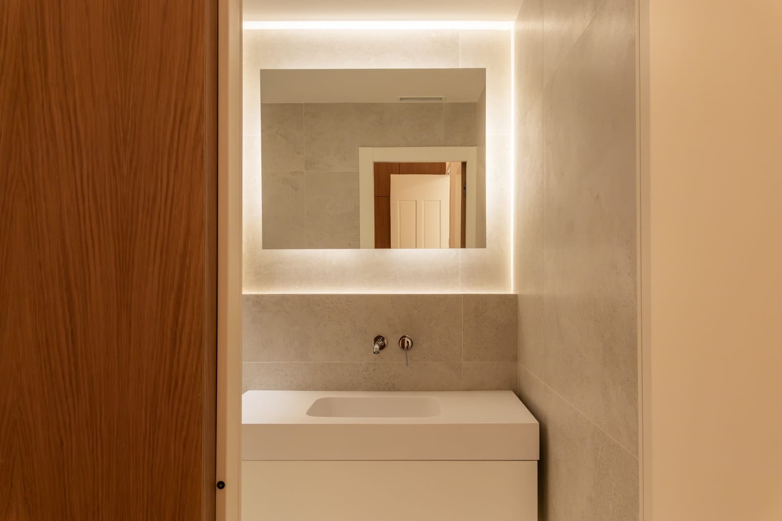 Baño en suite con espejo retroiluminado y lavabo integrado en encimera de Solid Surface