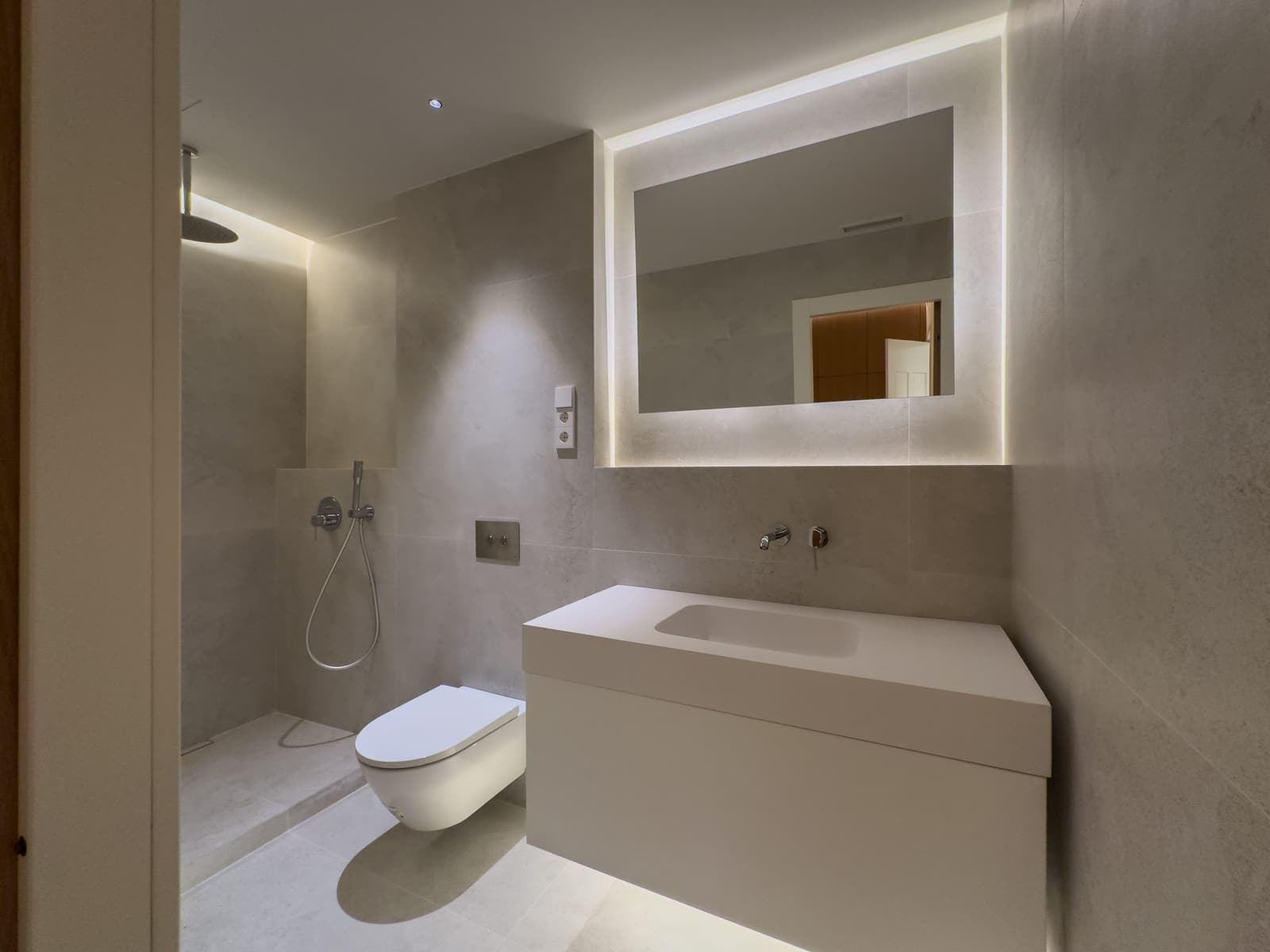 Baño con ducha de obra, inodoro suspendido y revestimiento porcelánico de tono claro