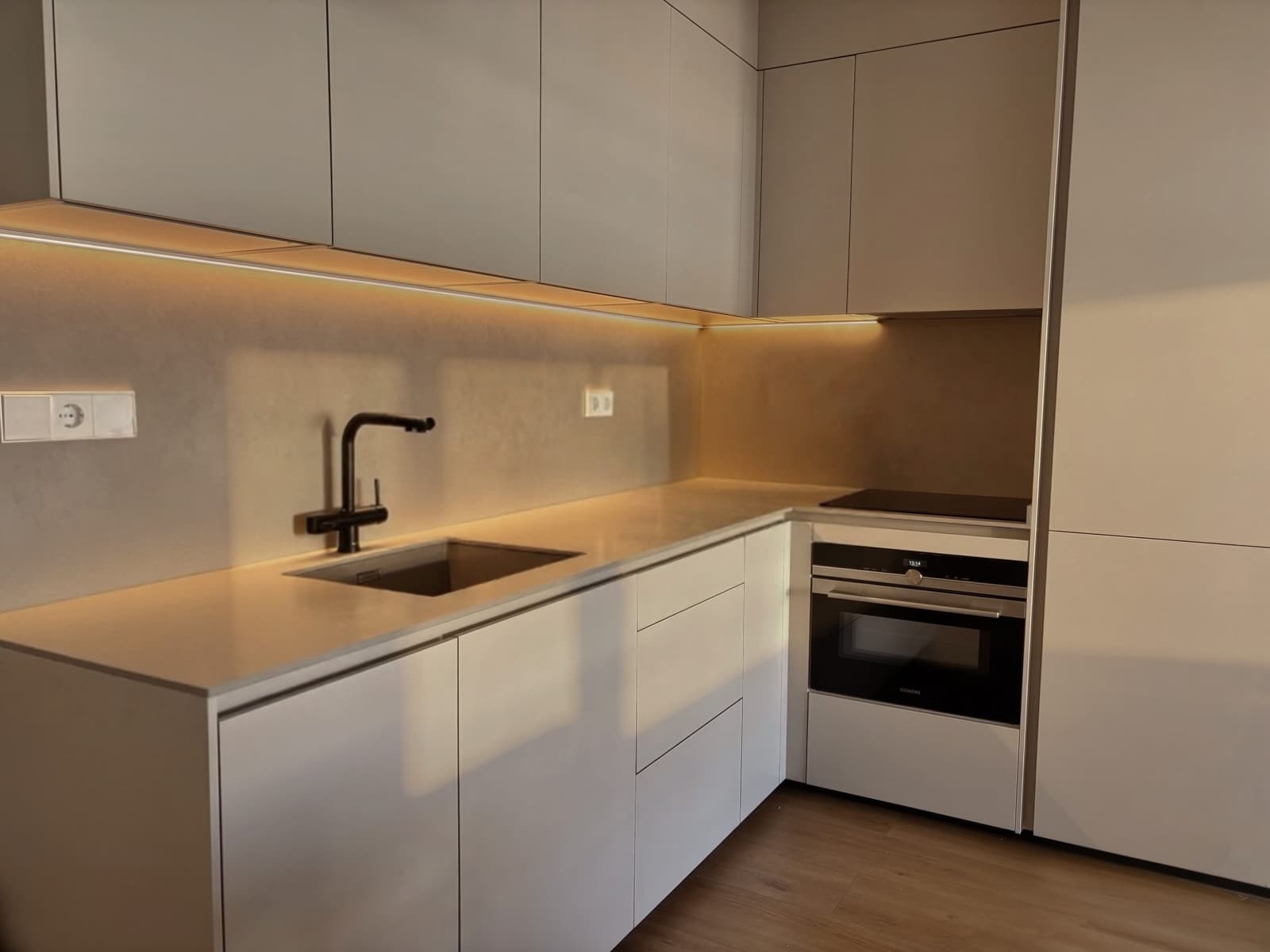 Cocina en L con frentes claros, encimera continua e iluminación bajo los muebles altos