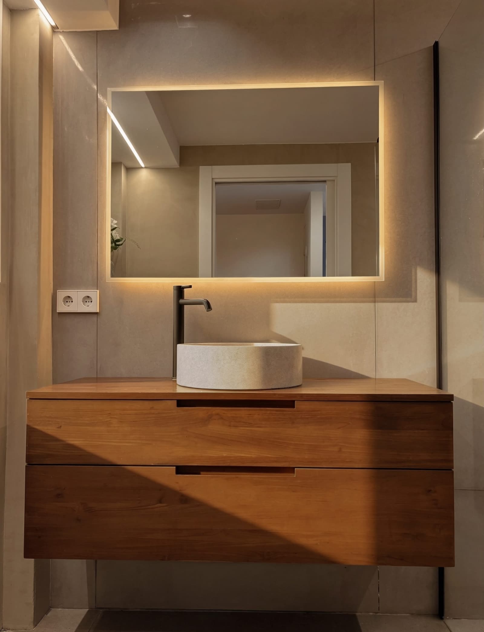 Baño con mueble de madera maciza, lavabo de piedra y espejo retroiluminado