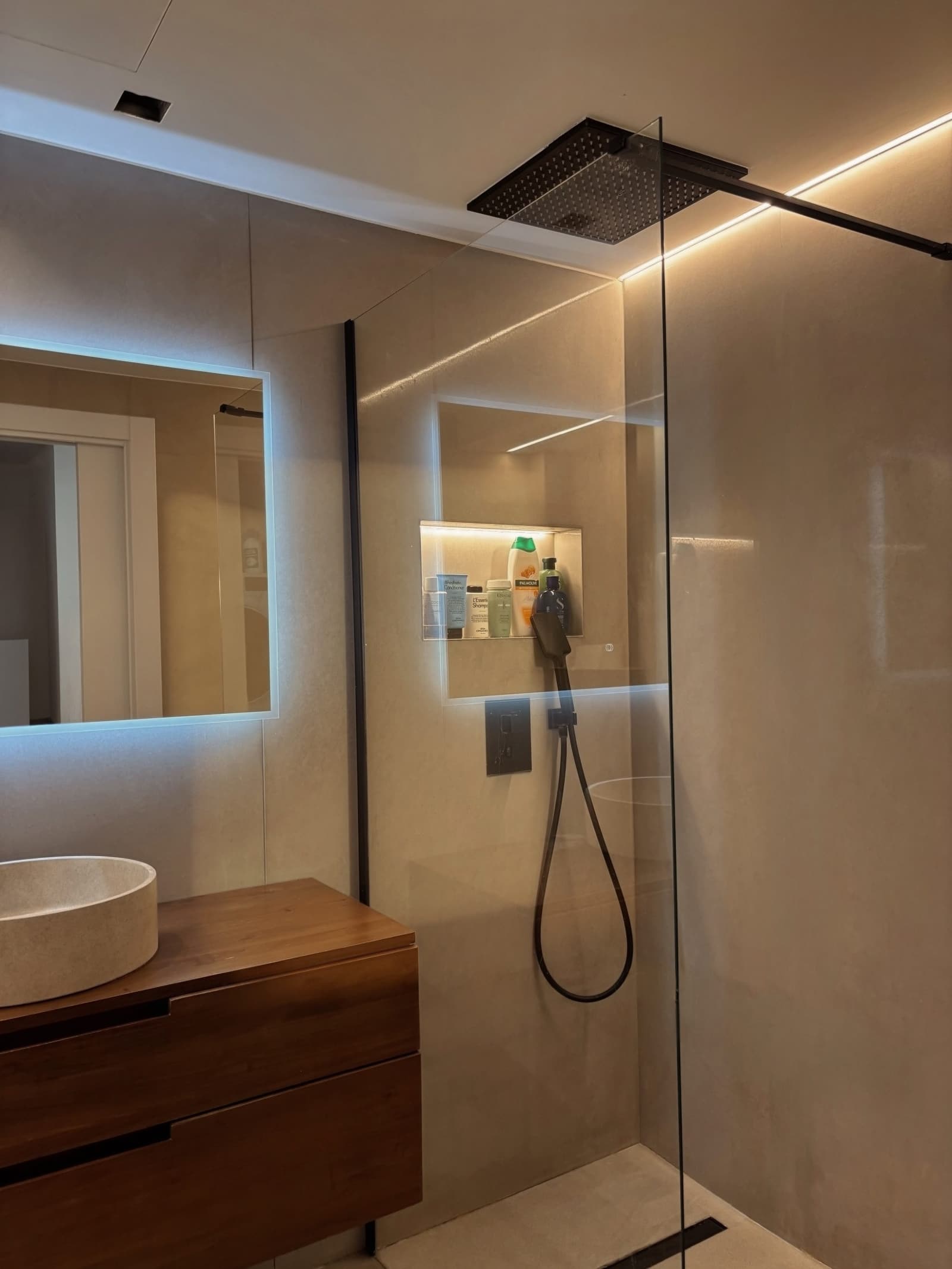 Ducha de obra con mampara de vidrio, hornacina retroiluminada y rociador de techo