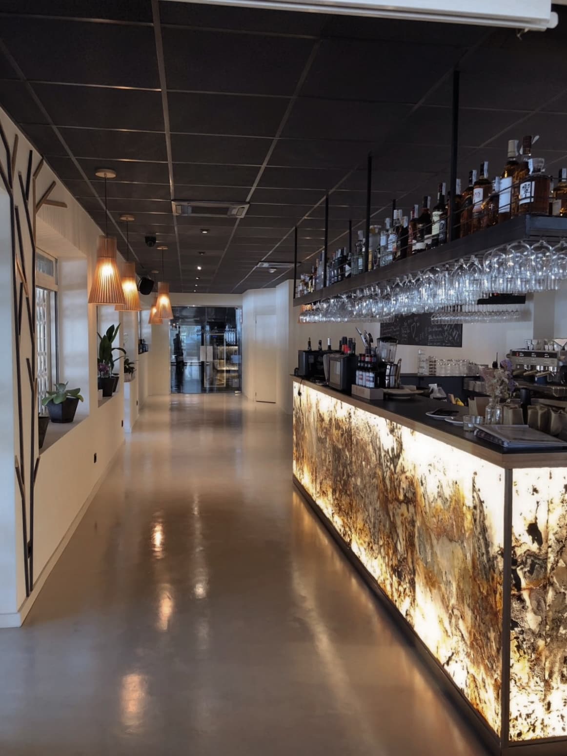 La sala en fuga hacia la barra retroiluminada, con el pavimento continuo y el techo oscuro