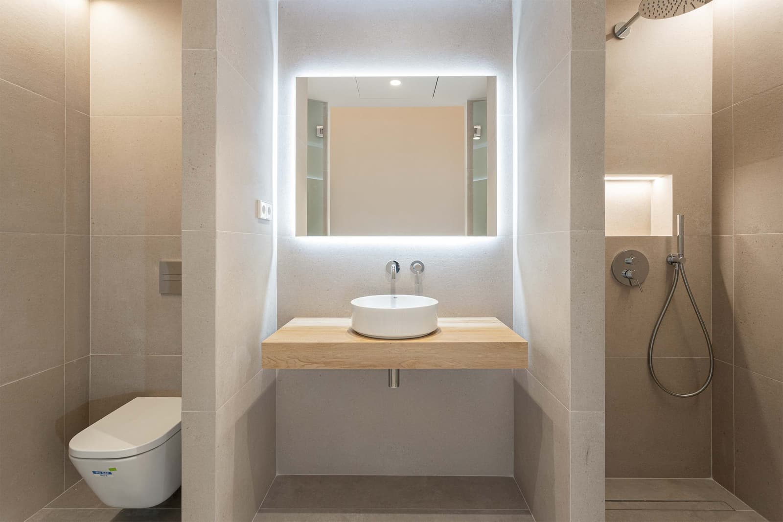 Baño con lavabo sobre repisa de roble, espejo retroiluminado y ducha de obra