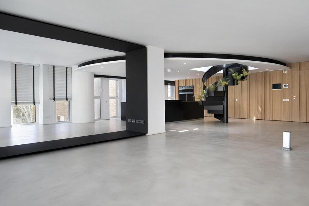 Espacio diáfano con el dintel metálico negro, los ventanales con estores y la cocina al fondo