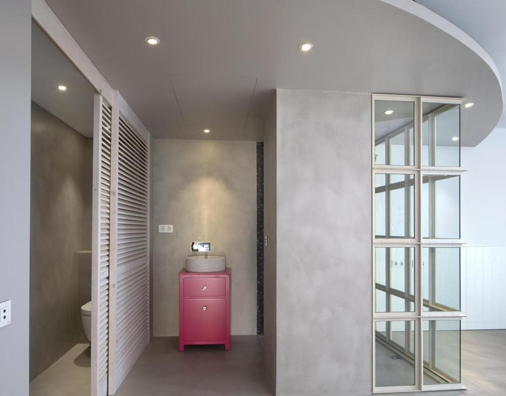 Aseo revestido de microcemento, con mueble en rosa y lavabo de piedra