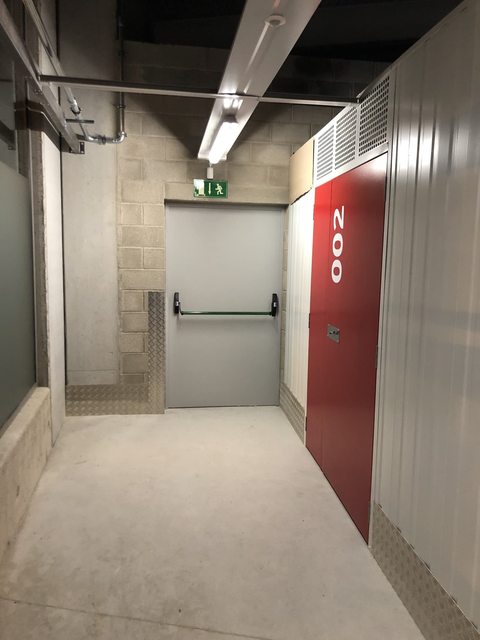 Pasillo de trasteros con los cerramientos metálicos modulares y la puerta cortafuegos con barra antipánico