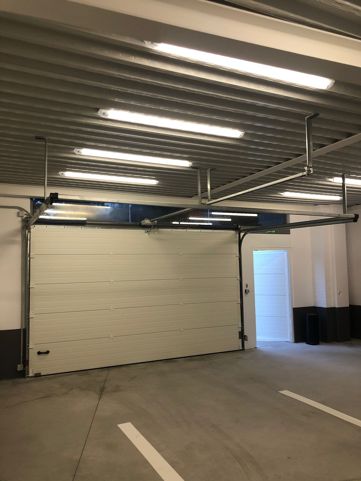 El garaje interior, con la puerta seccional, la estructura vista y las plazas marcadas en el pavimento