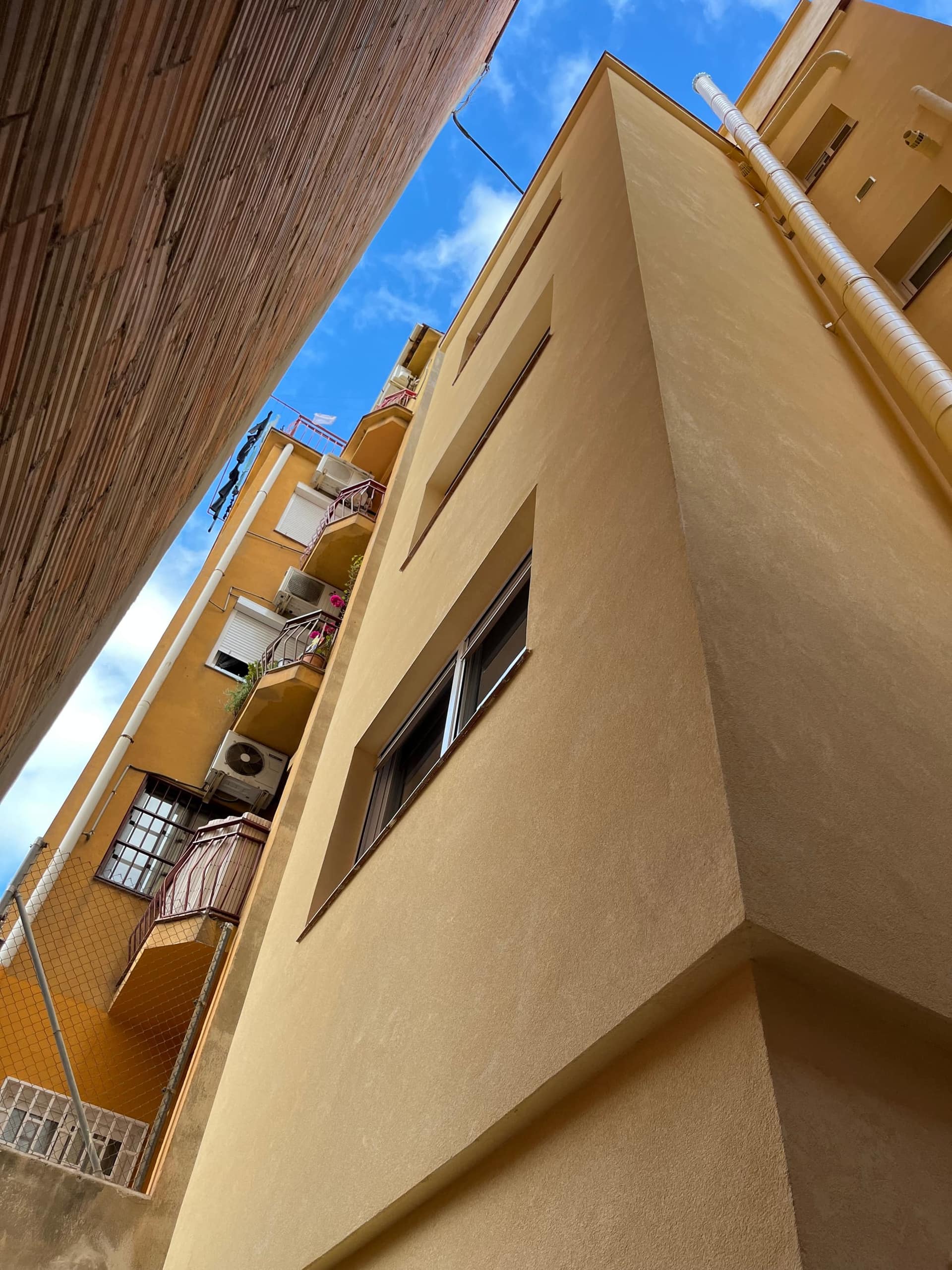 Contrapicado del patio de luces del edificio, con la fachada ya revestida de monocapa ocre junto a la finca vecina sin renovar
