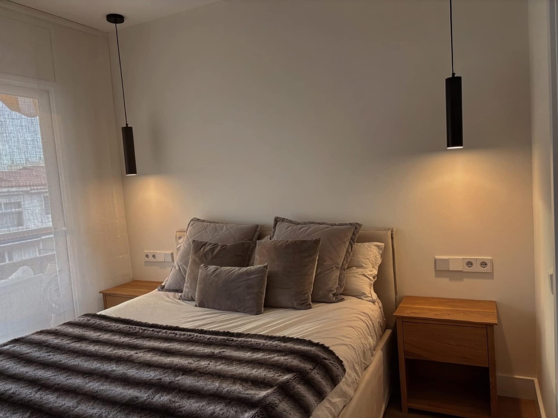 Dormitorio principal de Riu de l'Or, con cabecero tapizado, lámparas colgantes negras y mesitas de roble
